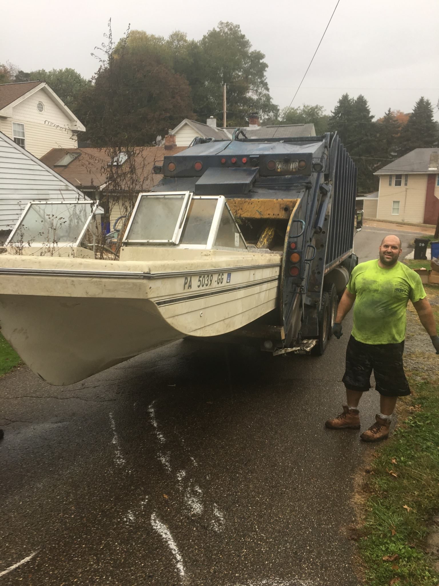 A man is standing next to a garbage truck with a boat in it.