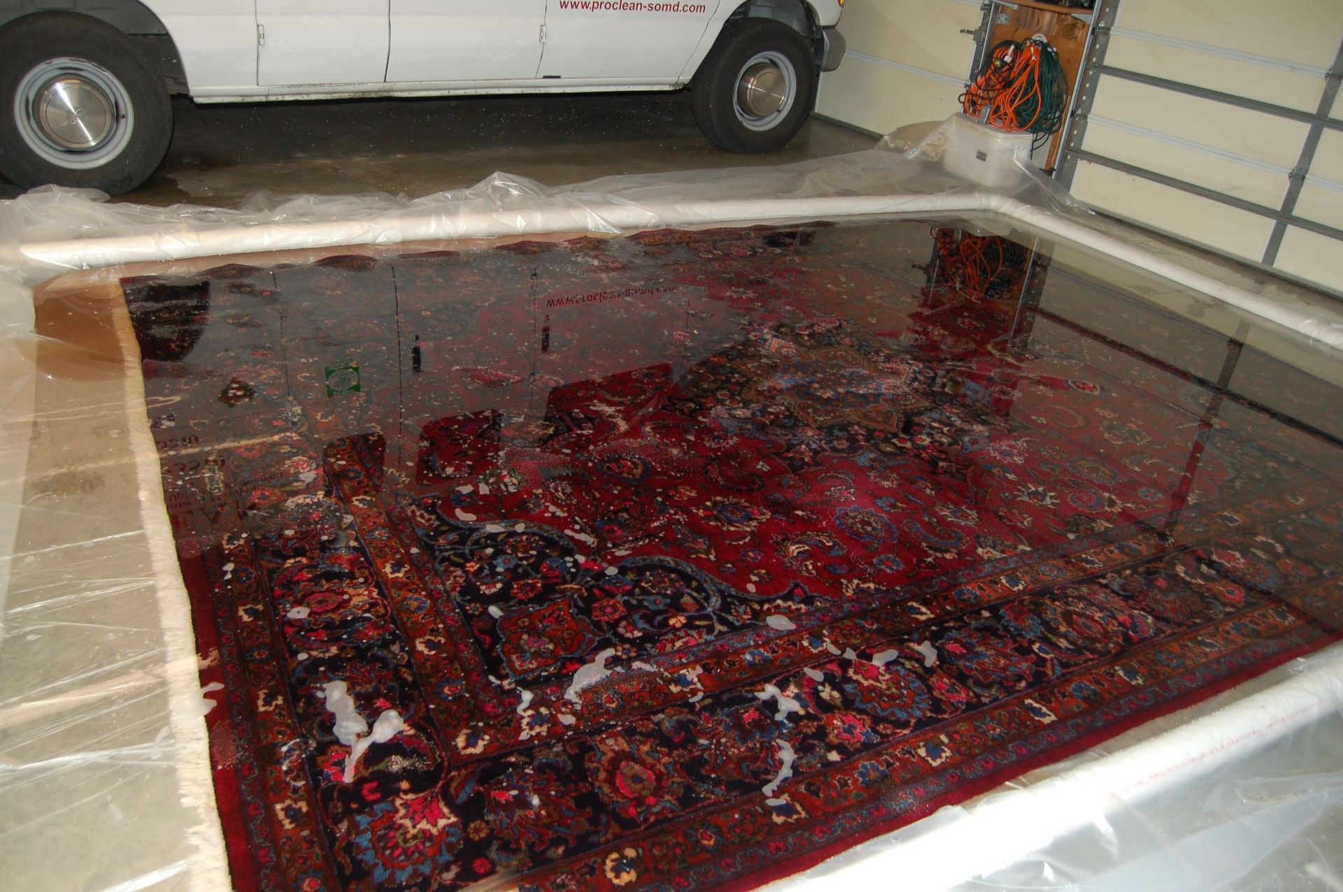 A white van is parked in a garage next to a large red rug.