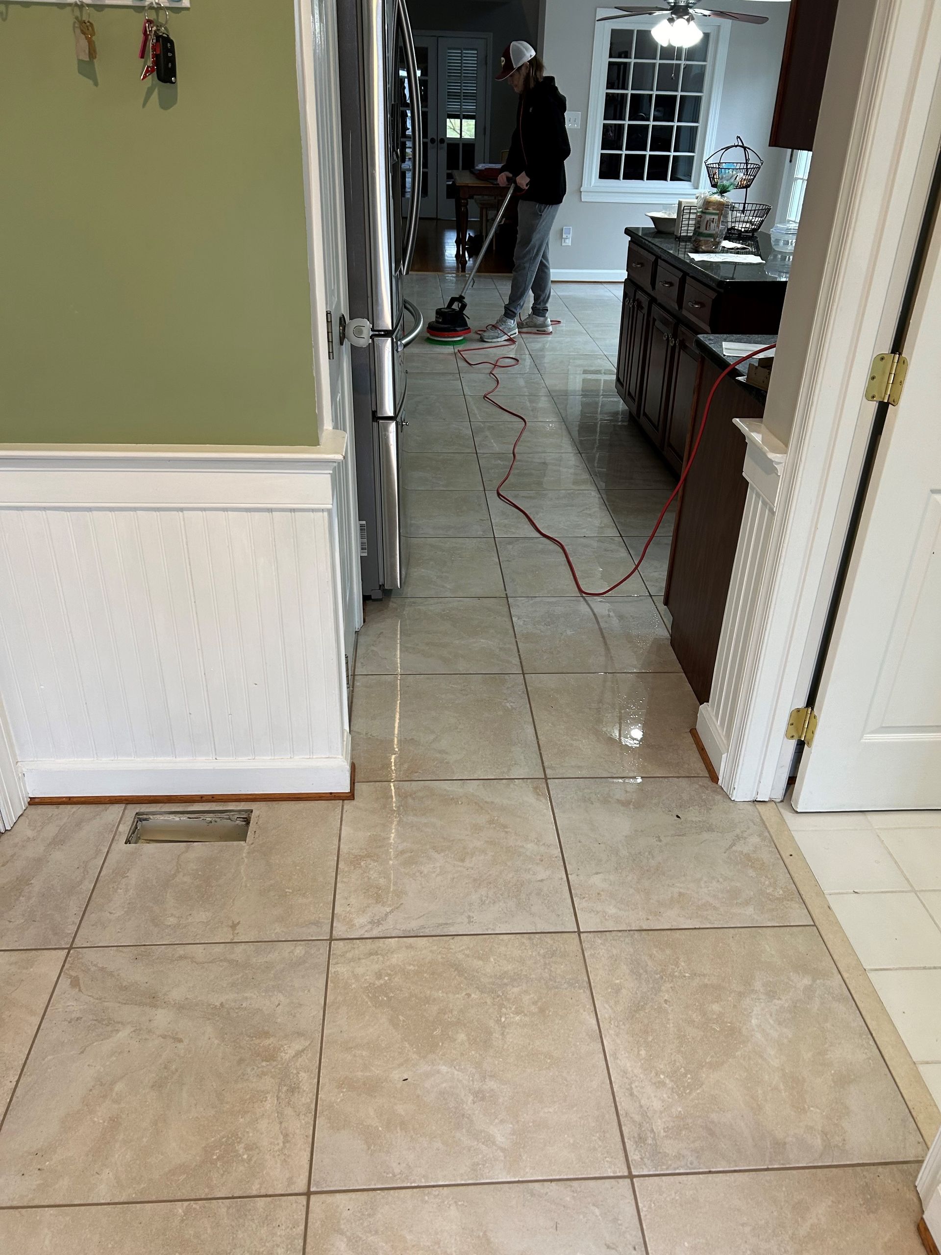 A man is vacuuming a tiled floor in a kitchen.