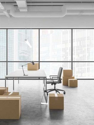 Office with desk, chair, and cardboard boxes. Large windows show a city view.