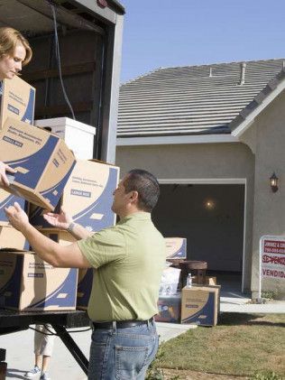People loading moving boxes into a truck outside a house with an open garage.
