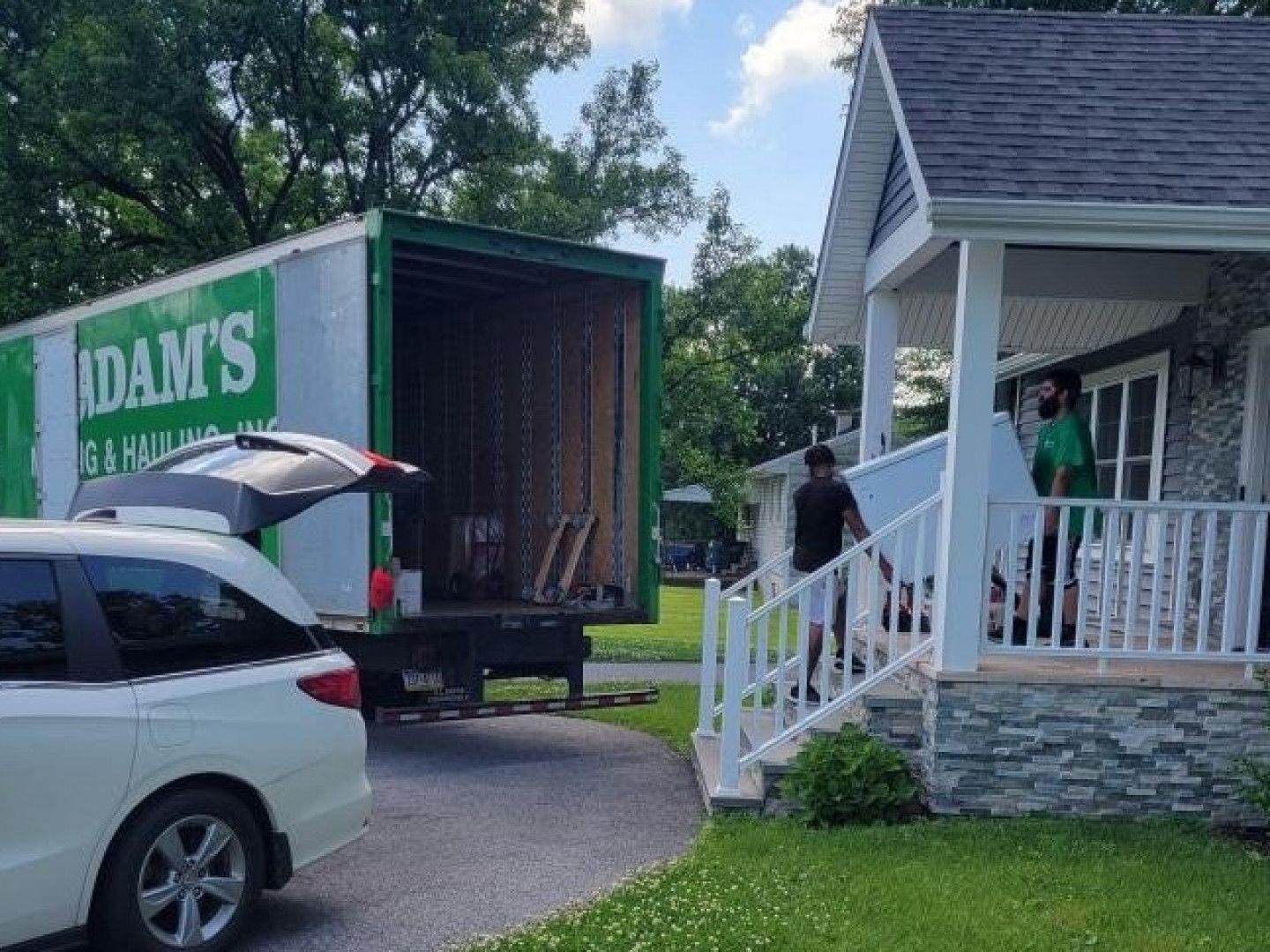 Moving truck parked next to a house, men carrying furniture from porch into the truck.