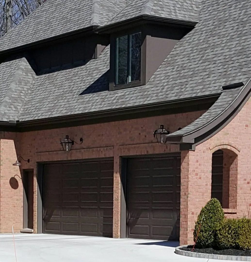 A brick house with two garage doors and a gray roof