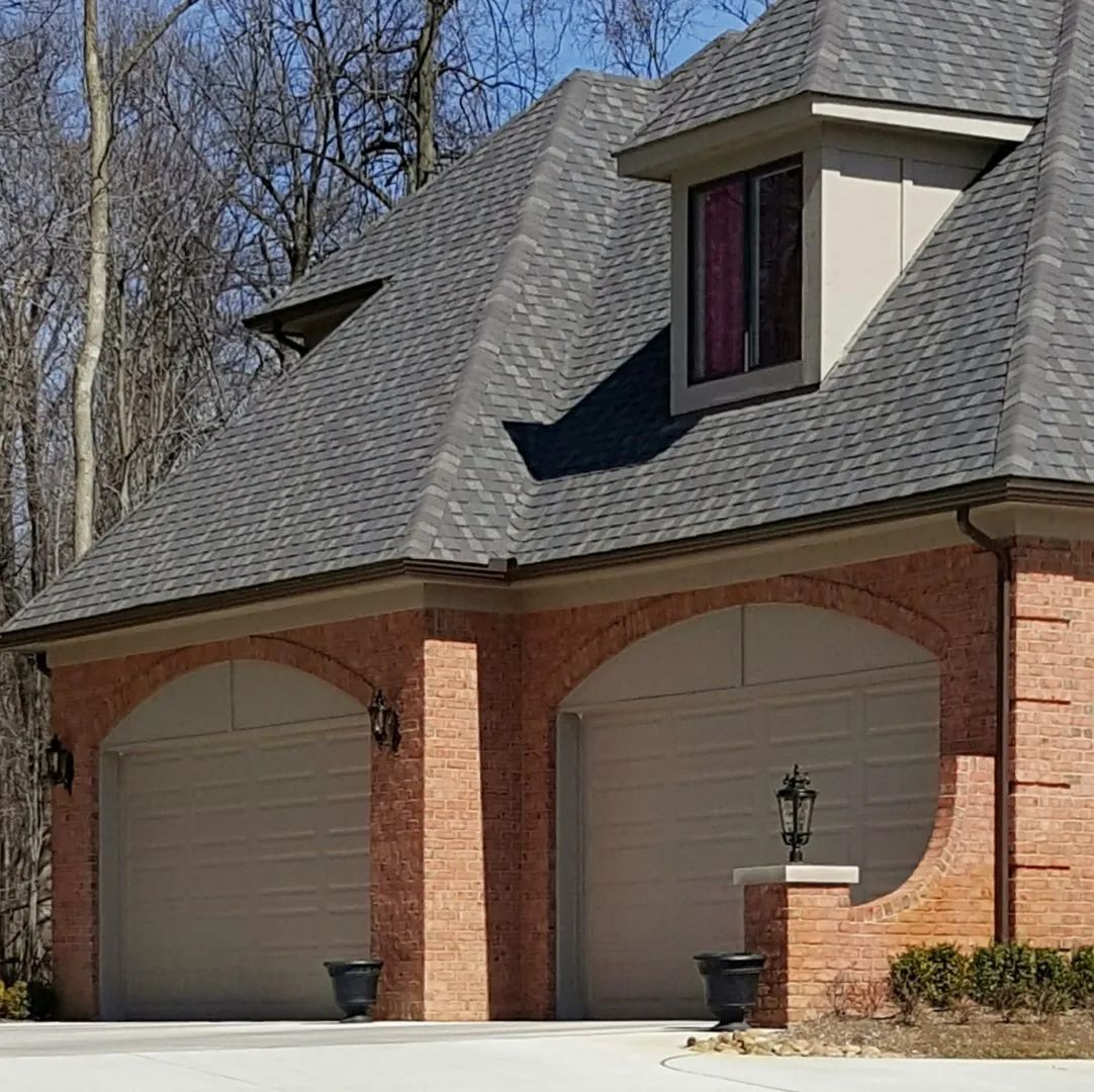 A brick house with two garage doors and a gray roof