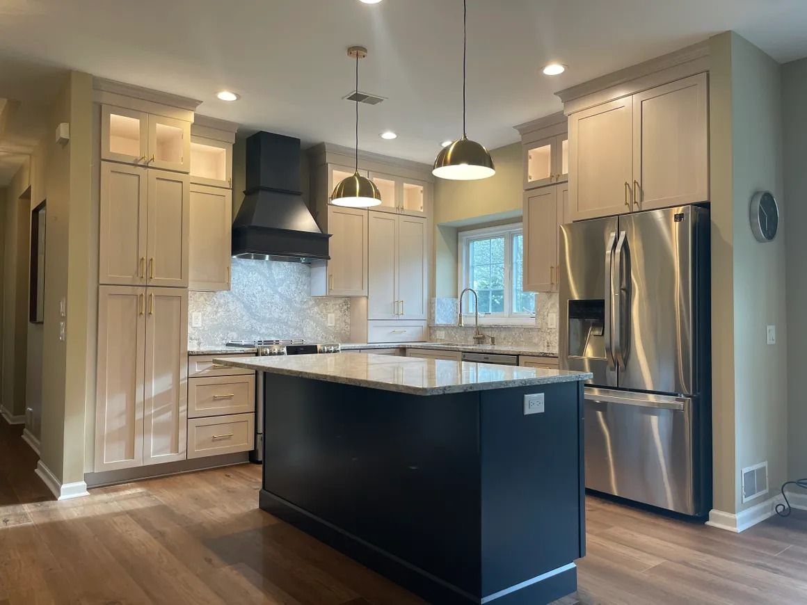 Modern kitchen with dark blue island, stainless steel appliances, and light cabinets.