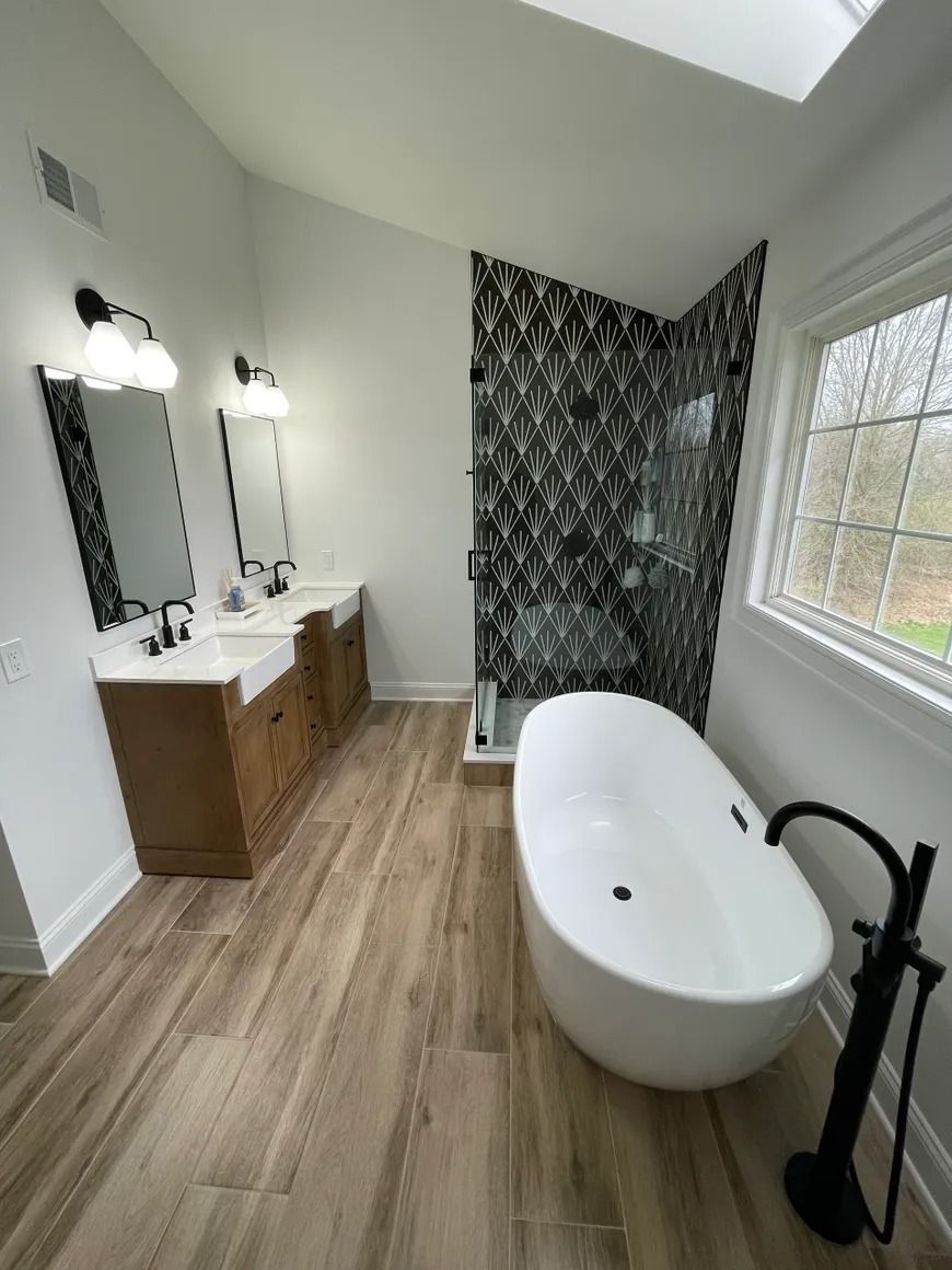 Modern bathroom with wood-look tile, double vanity, black accent wall, freestanding tub, and shower.