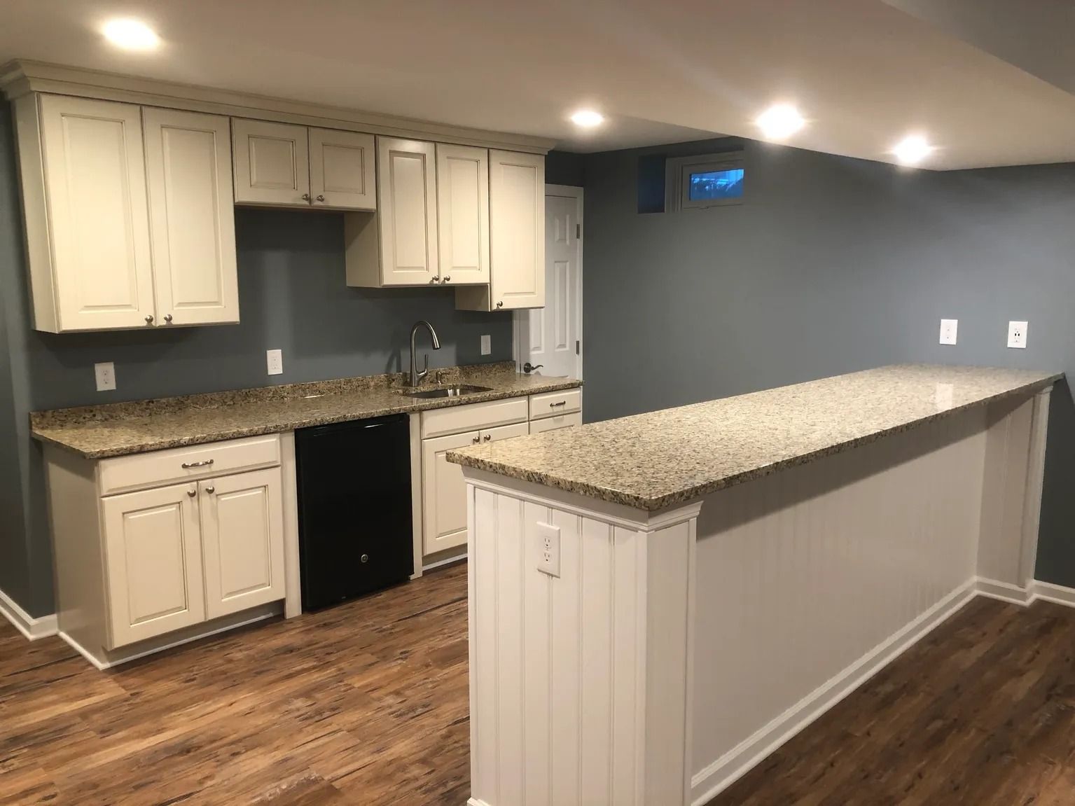 Kitchen area with cream cabinets, granite countertops, and a bar with wood-look flooring and gray walls.