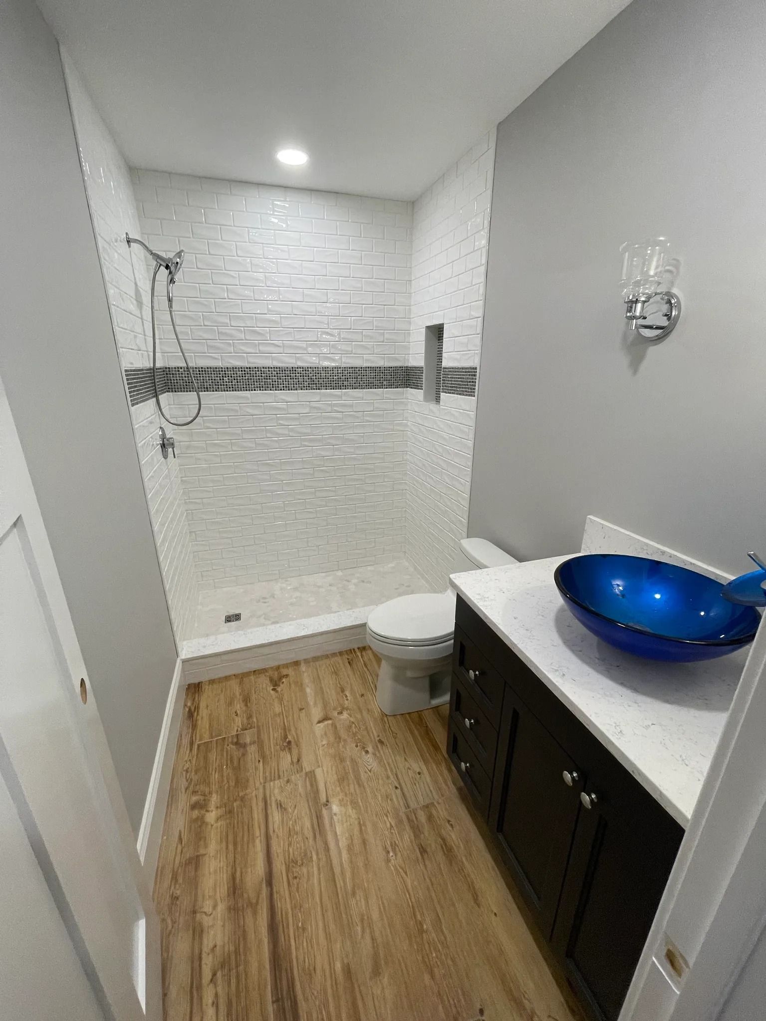 Bathroom with a blue whale-shaped sink, shower with white and dark tile, and dark wood-look floor.