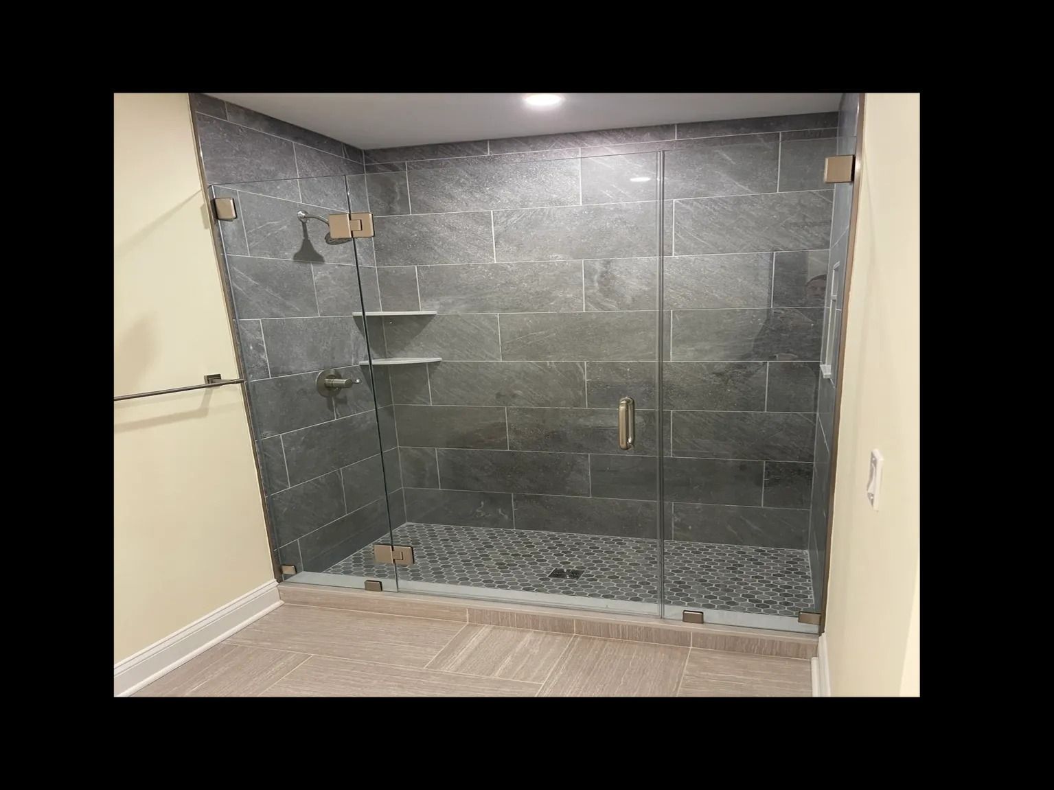 Modern shower with gray stone walls, glass doors, and pebble floor.
