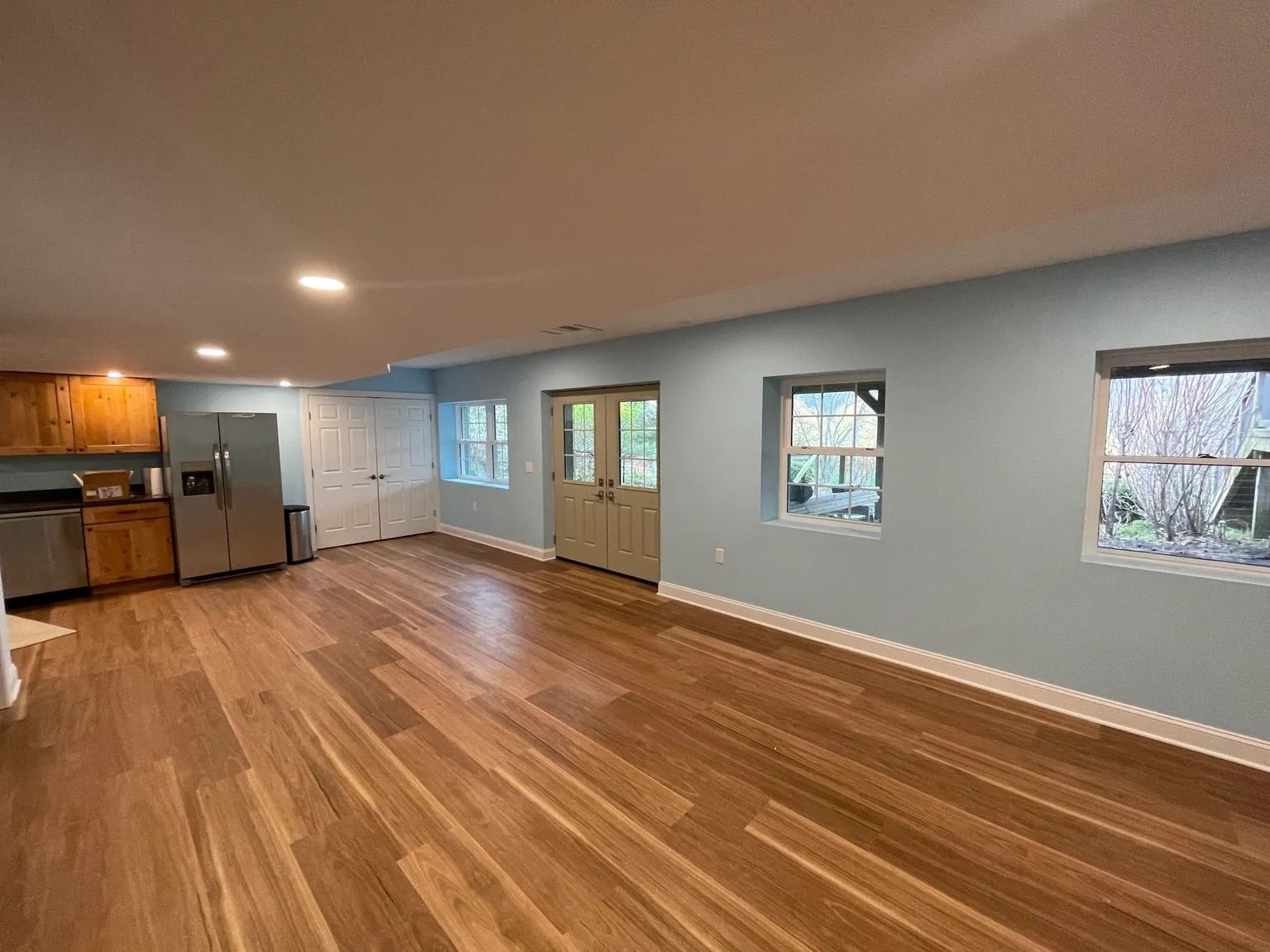 Spacious room with wood flooring, light blue walls, kitchen with stainless steel appliances, and French doors.