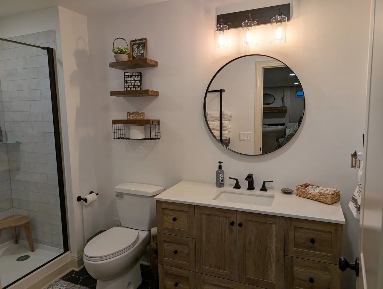 Bathroom with wooden vanity, round mirror, and floating shelves.