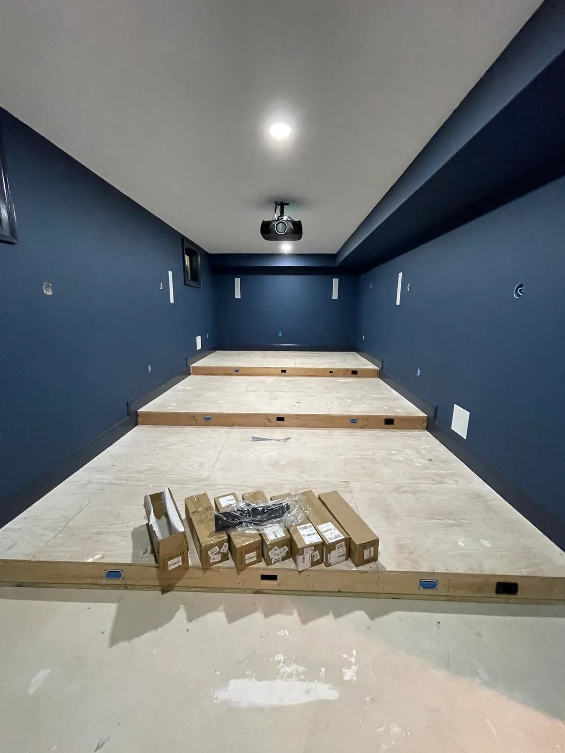 A home theater under construction with blue walls, tiered flooring, a projector, and boxes of equipment.