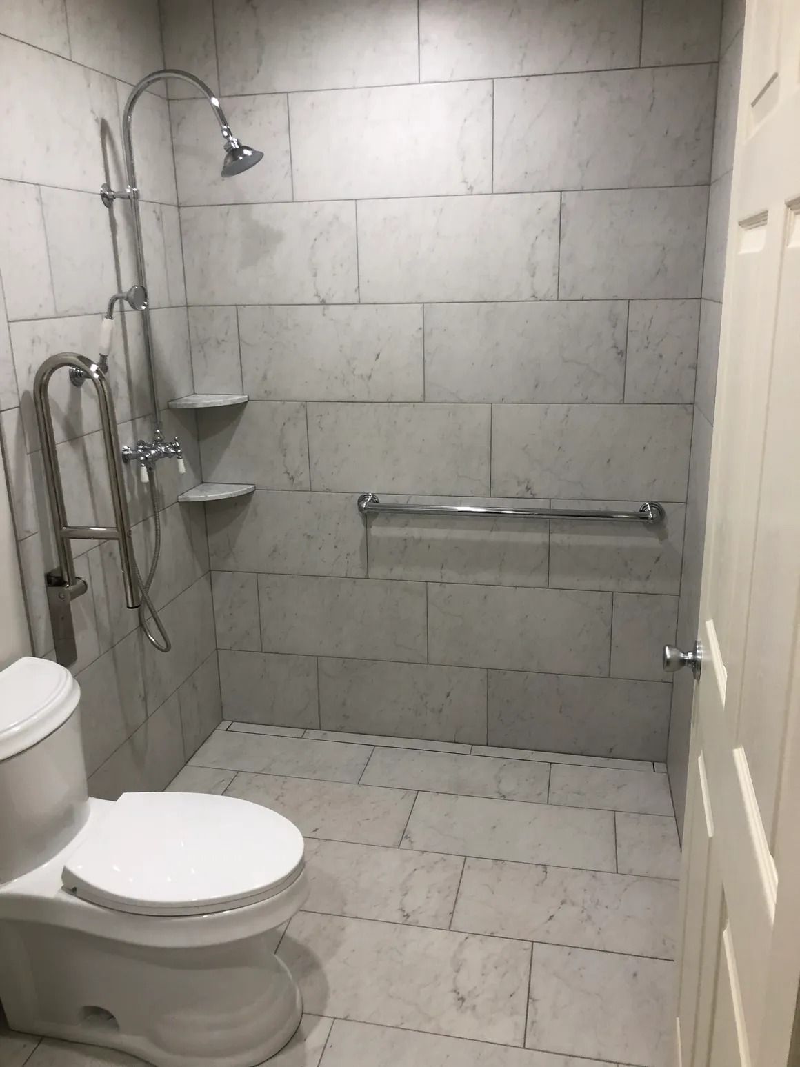Accessible bathroom with tiled walls and floor, shower, grab bars, and toilet.