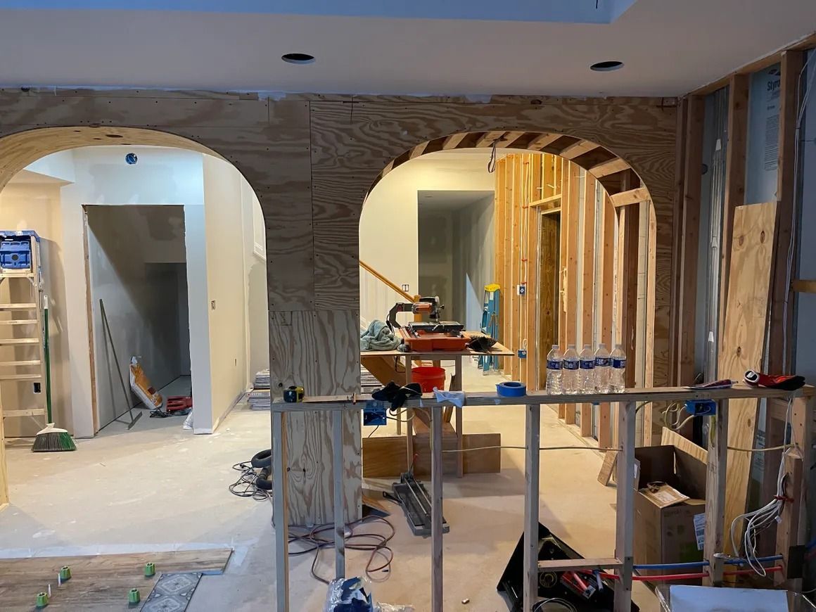 Interior construction in progress, arched doorways. Wood framing, drywall, and tools visible.