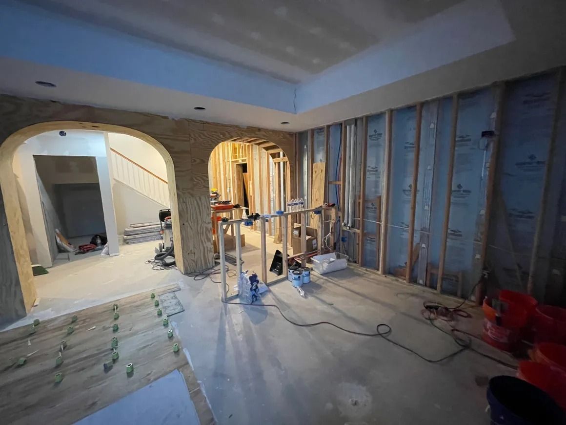 Interior construction site: framing, archways, exposed insulation, electrical wiring, and a partially finished floor.