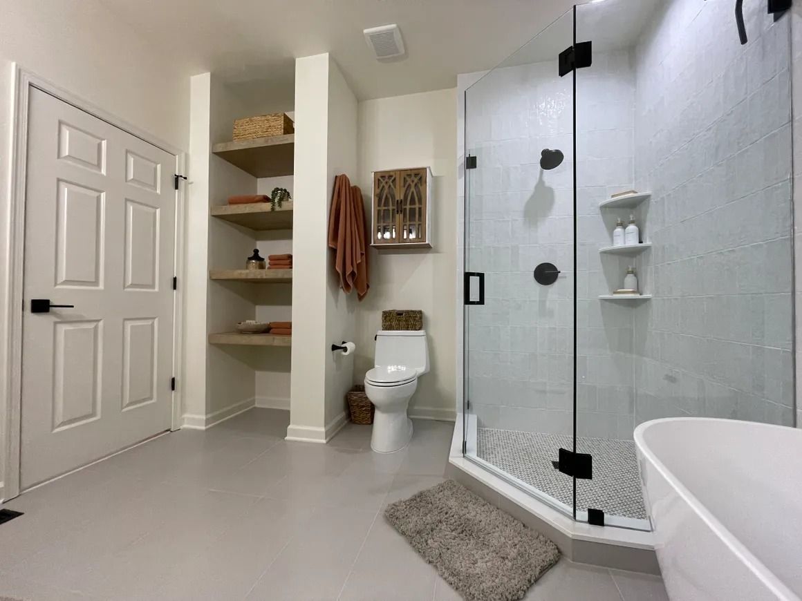 Bathroom with white walls, shower, shelves, and toilet; gray floor; neutral decor.
