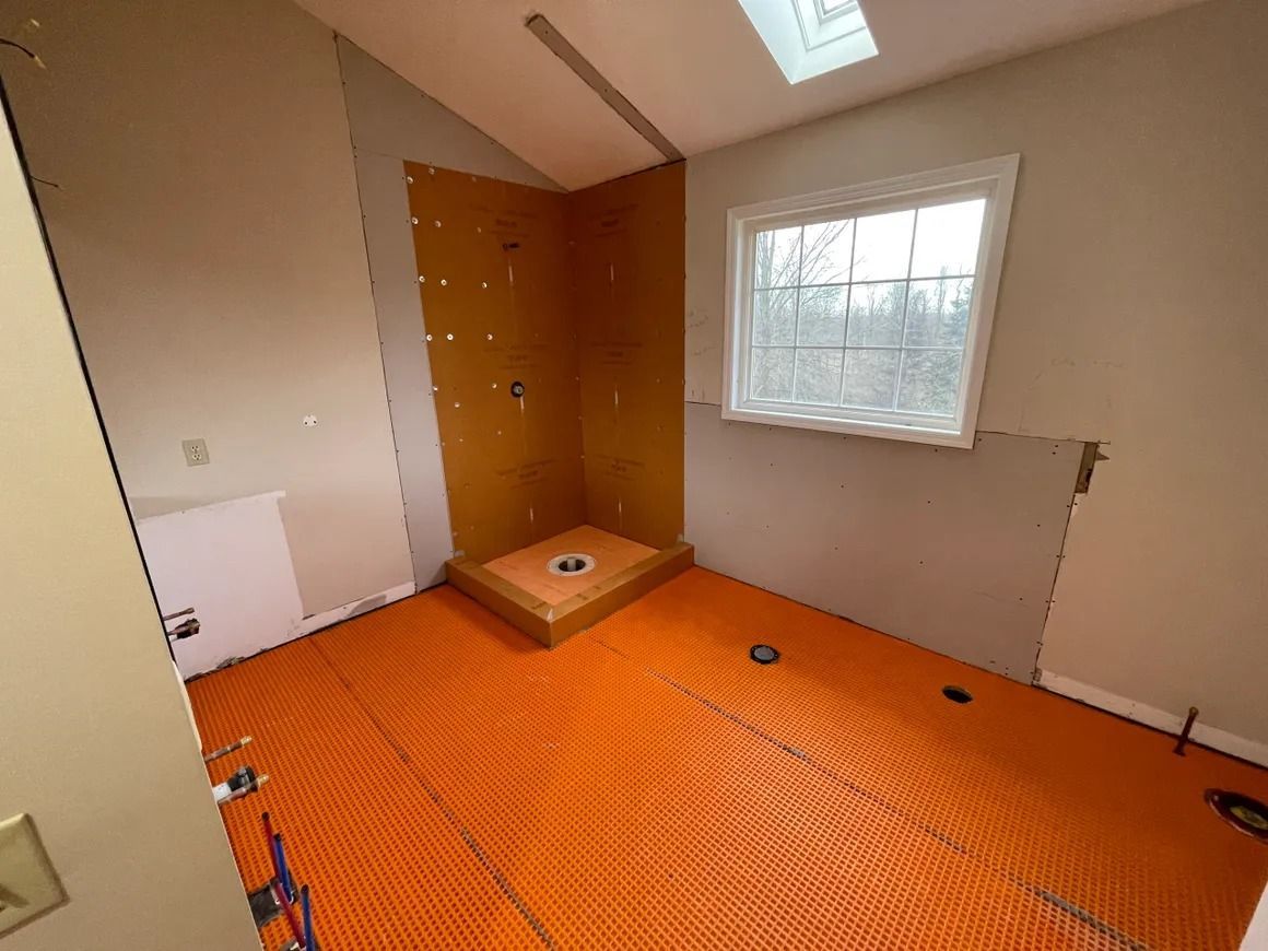 Bathroom under construction with orange radiant floor heating, shower stall, and window.