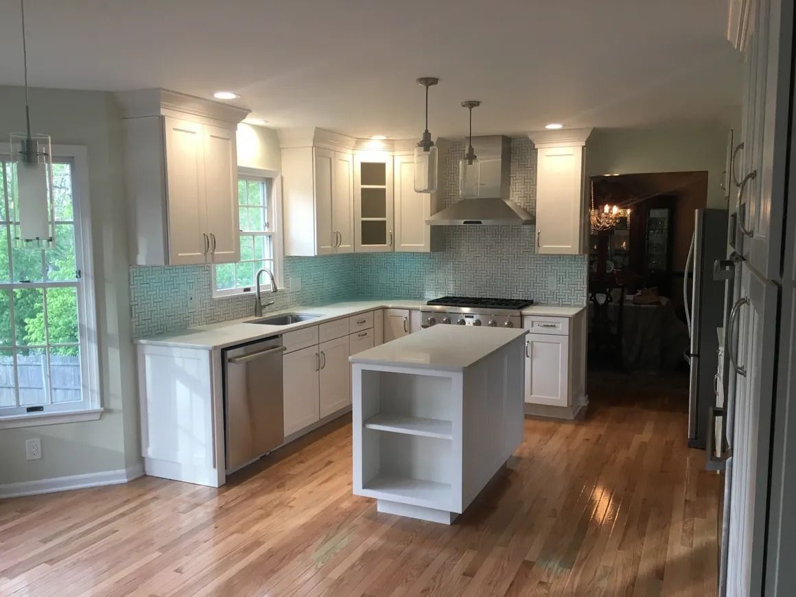 White kitchen with stainless steel appliances, teal backsplash, and wood floors.