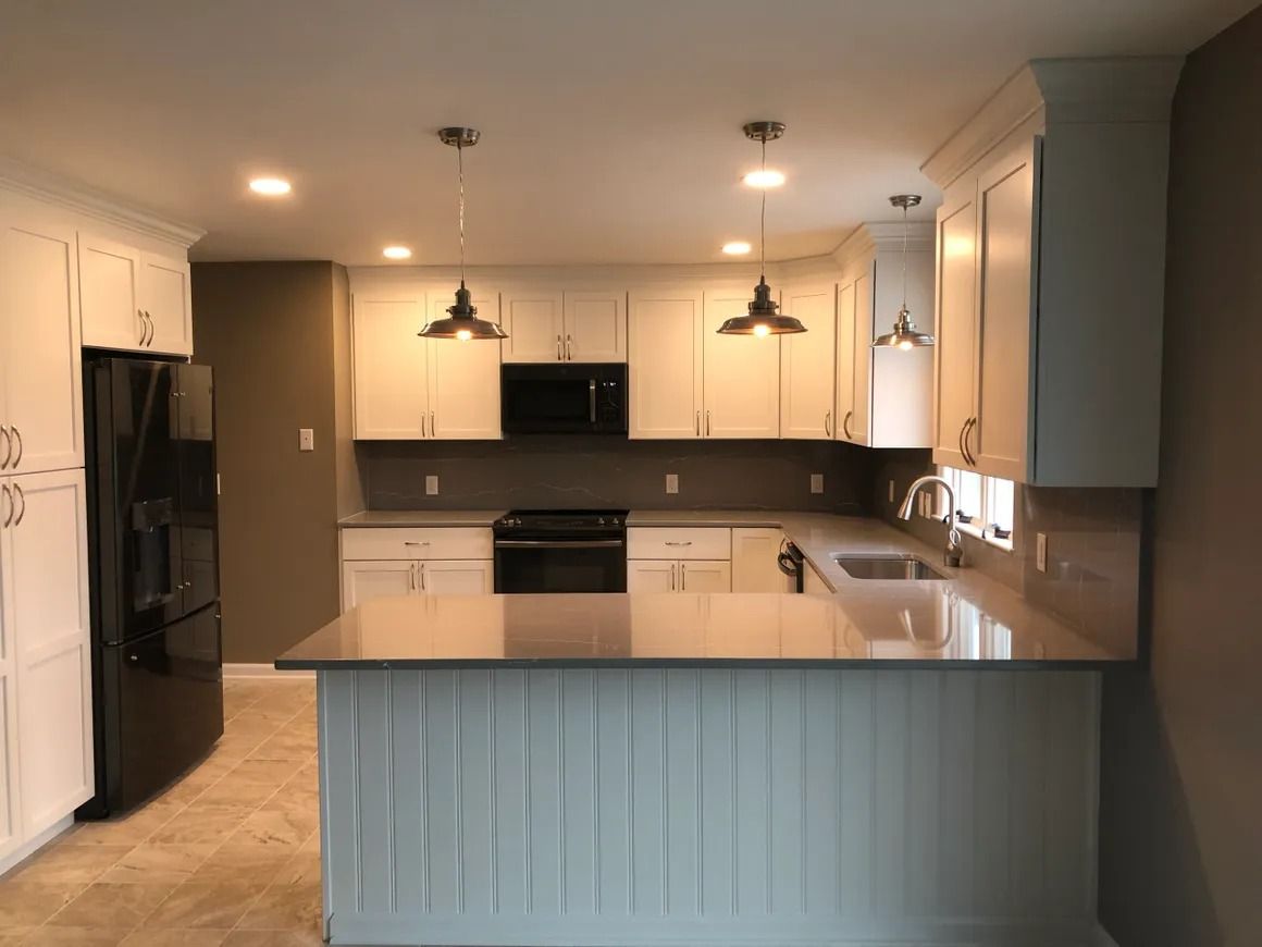 White kitchen with black appliances, gray countertops, and pendant lights.
