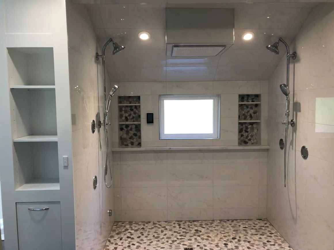 Spacious shower with pebble floor, multiple shower heads, built-in shelving, and a small window.