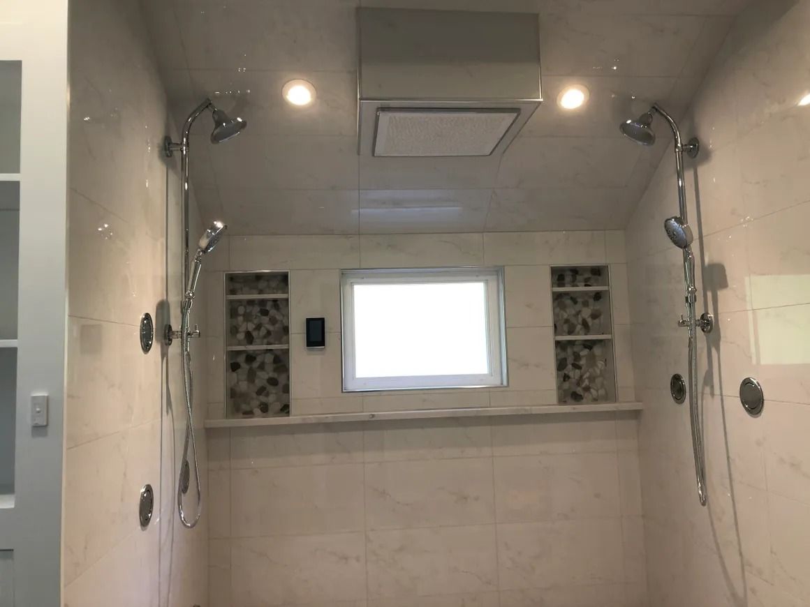 A luxurious, tiled shower with two shower heads, a window, and recessed stone niches.