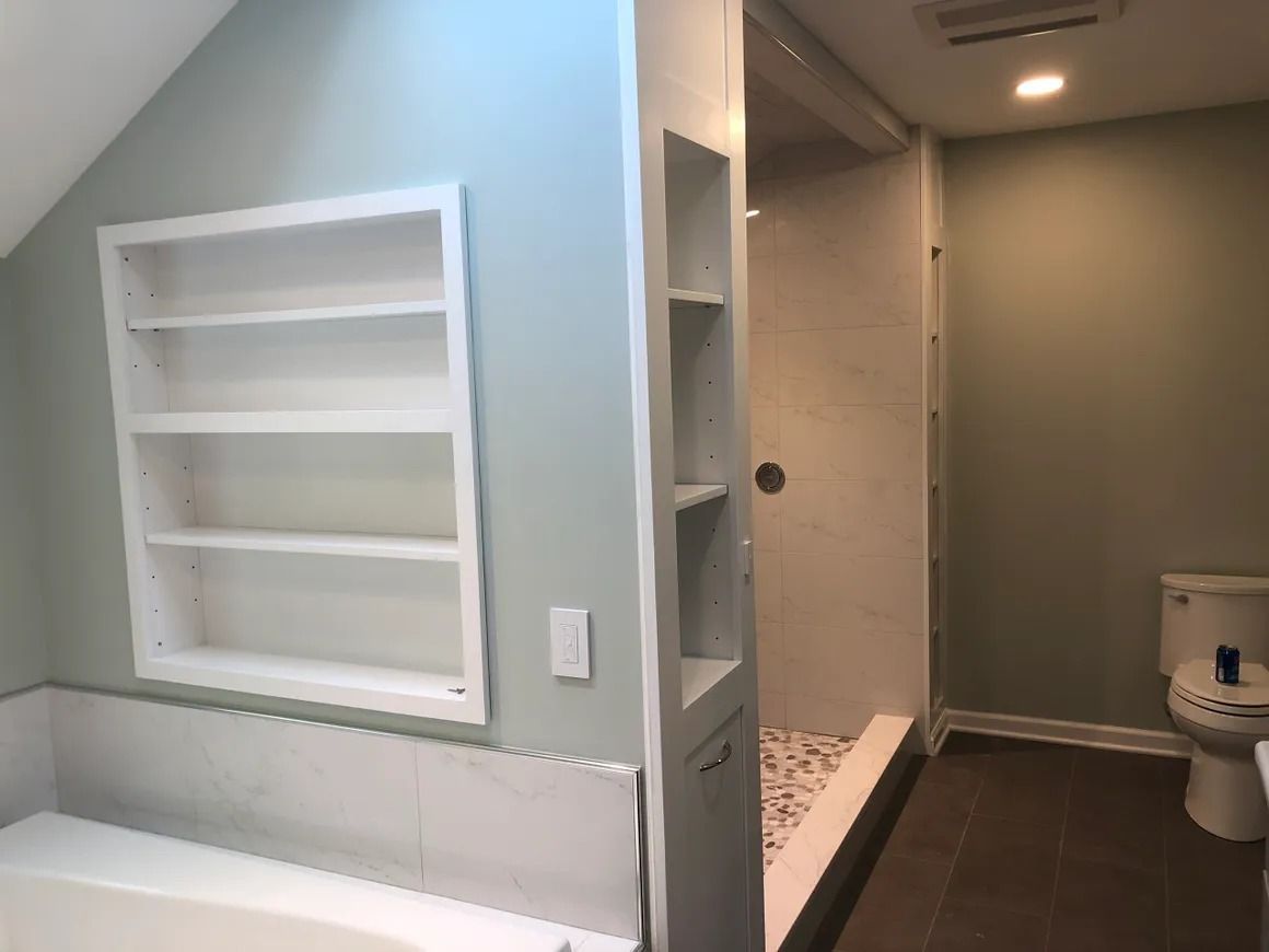 Bathroom with built-in shelves, white tile, shower, and toilet, painted green walls.