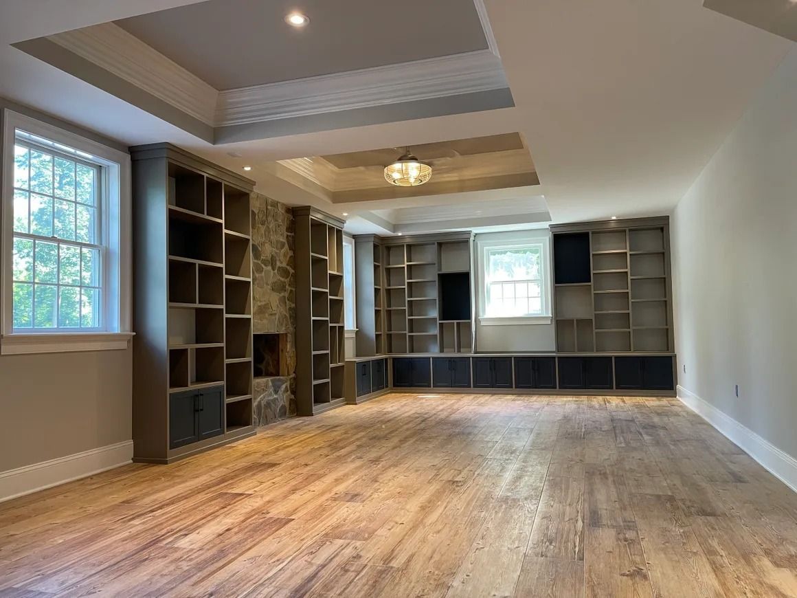 Empty room with built-in bookshelves, fireplace, and wood flooring. Light fixtures and windows.