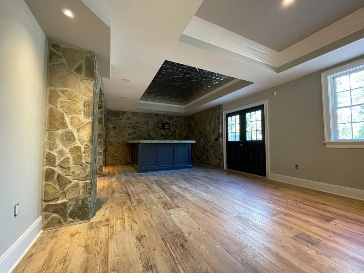 Interior with stone walls, wooden floor, bar, black double doors, and window.