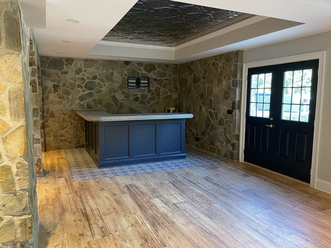 Interior with a stone wall and bar; blue cabinets, wood floor and black double doors.