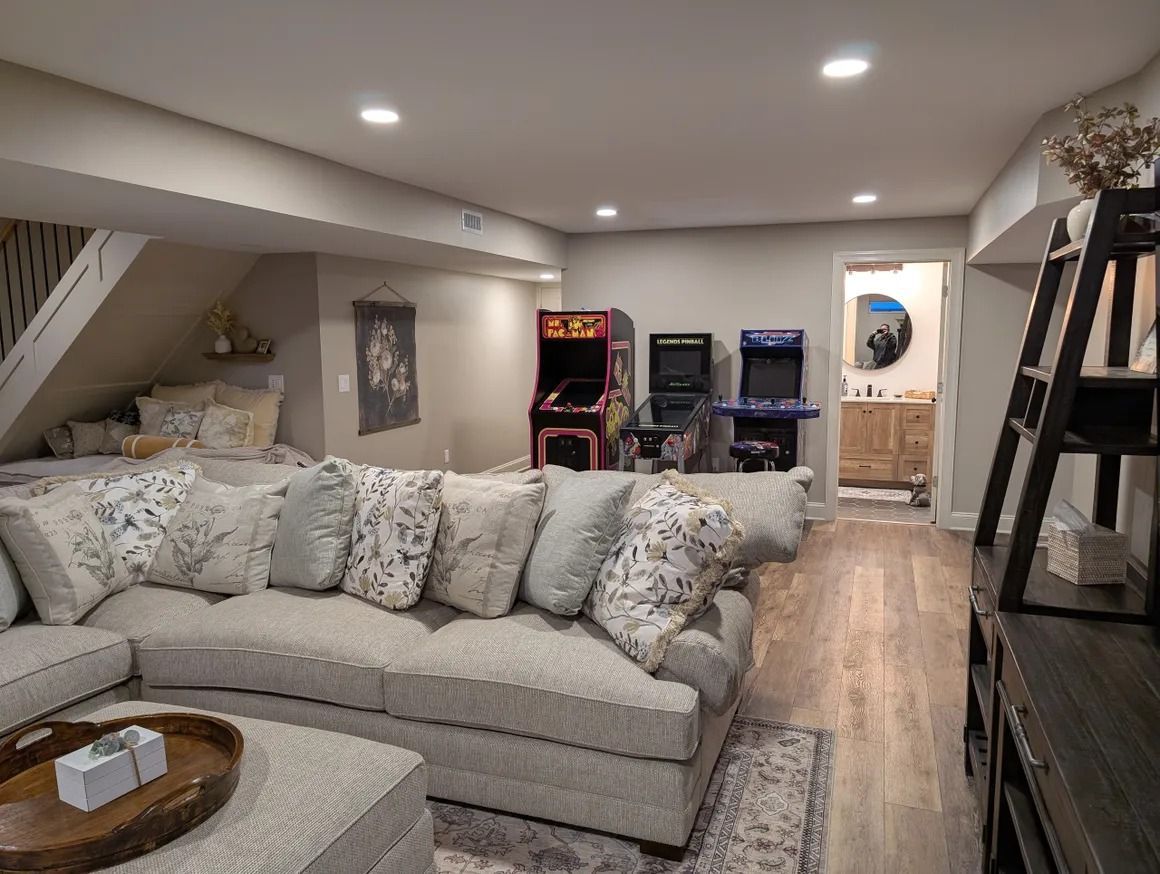 Cozy basement with a large sectional sofa, arcade games, and a bathroom visible down the hall.