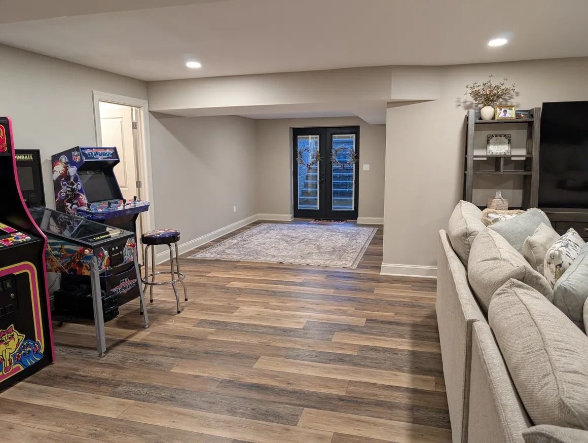 Basement with arcade games, sofa, rug, and dark double doors leading outside.
