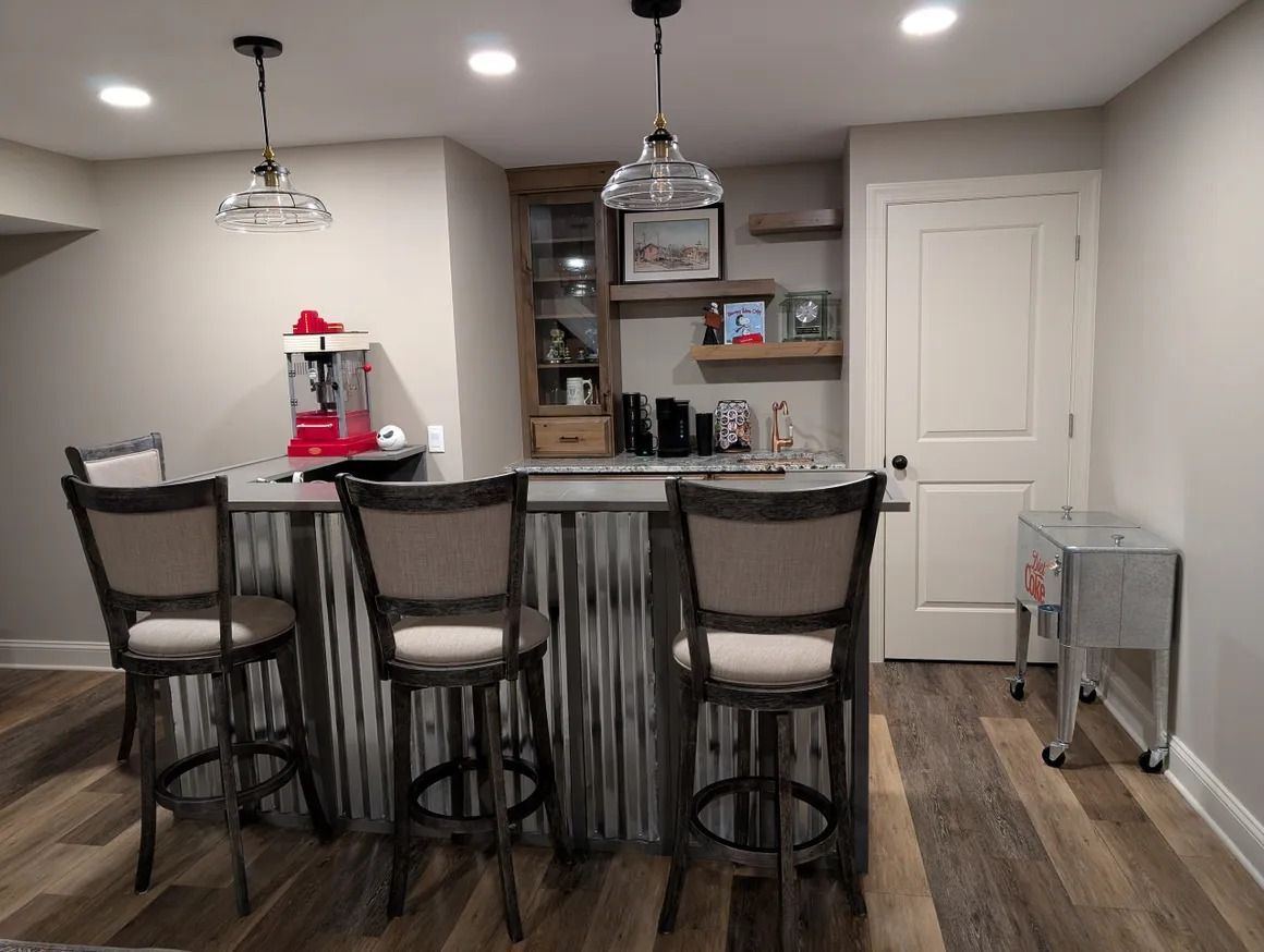 Bar area with corrugated metal facade, three bar stools, wooden shelves, and a popcorn maker.