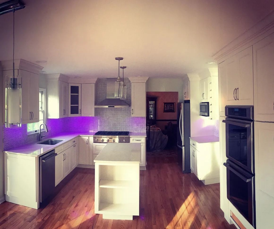 Bright white kitchen with purple under-cabinet lighting. Features include a center island, stainless appliances, and hardwood floors.