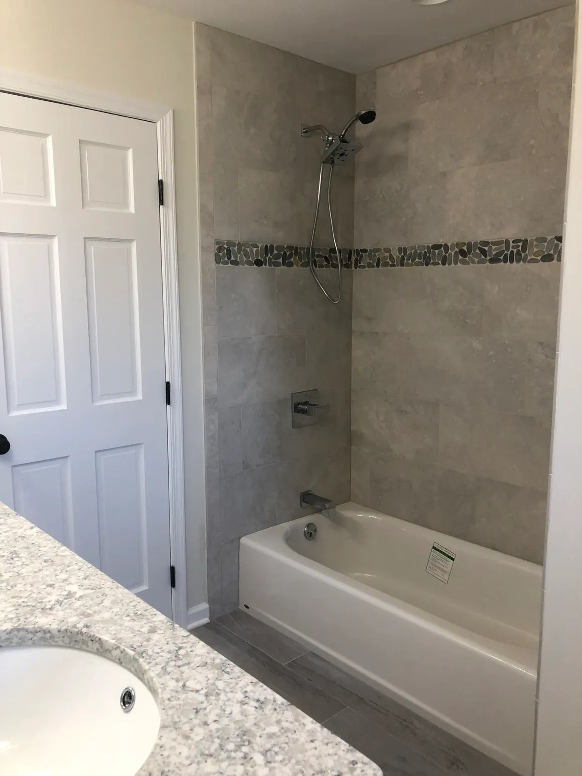 Bathroom with tiled shower, white tub, gray walls, vanity and door.