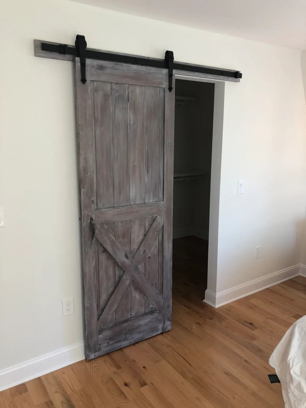 Gray barn door on a black track, leading to a white-walled closet, set on hardwood floors.