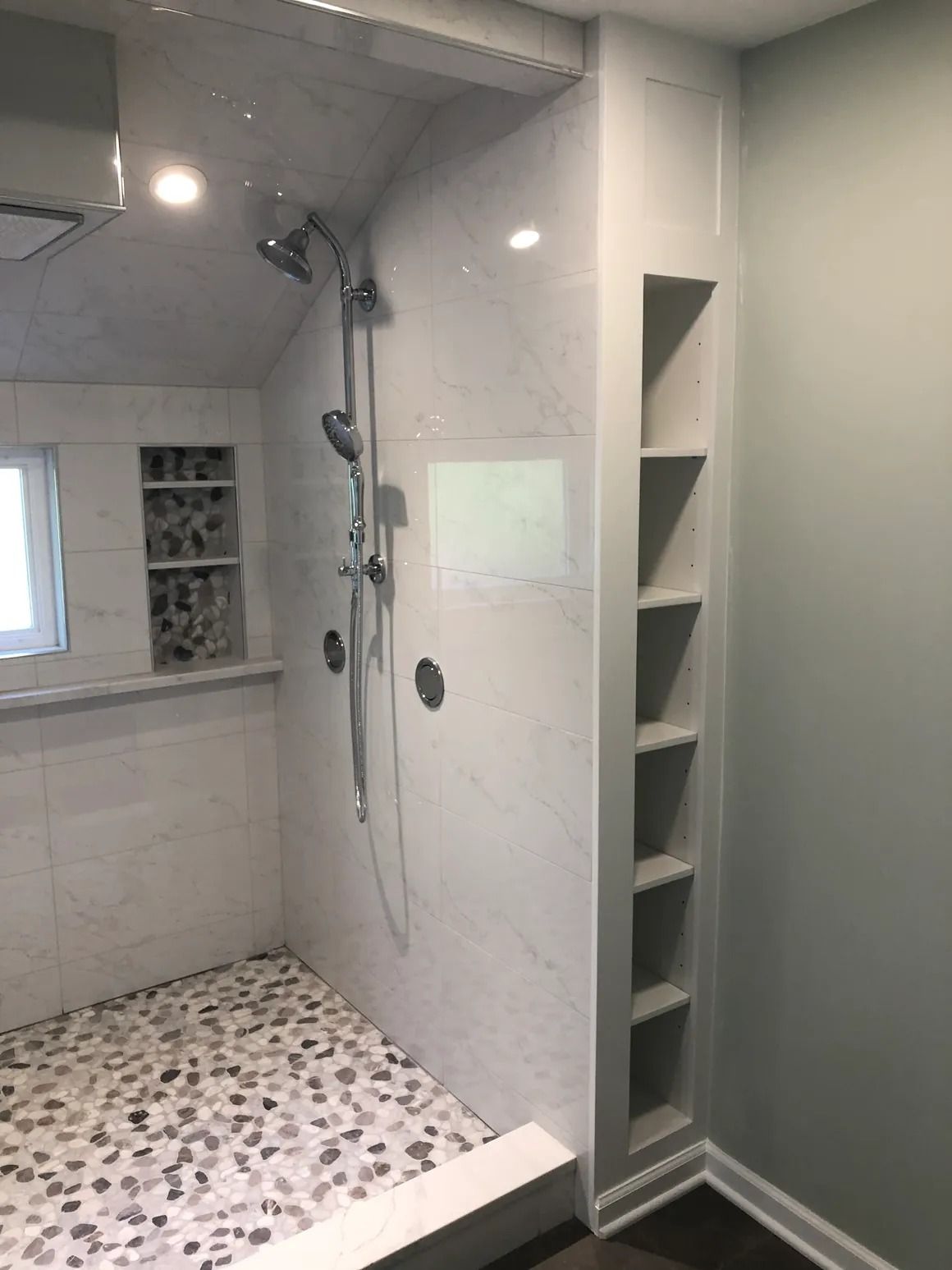 Bathroom shower with white marble walls, pebble floor, and built-in shelving.