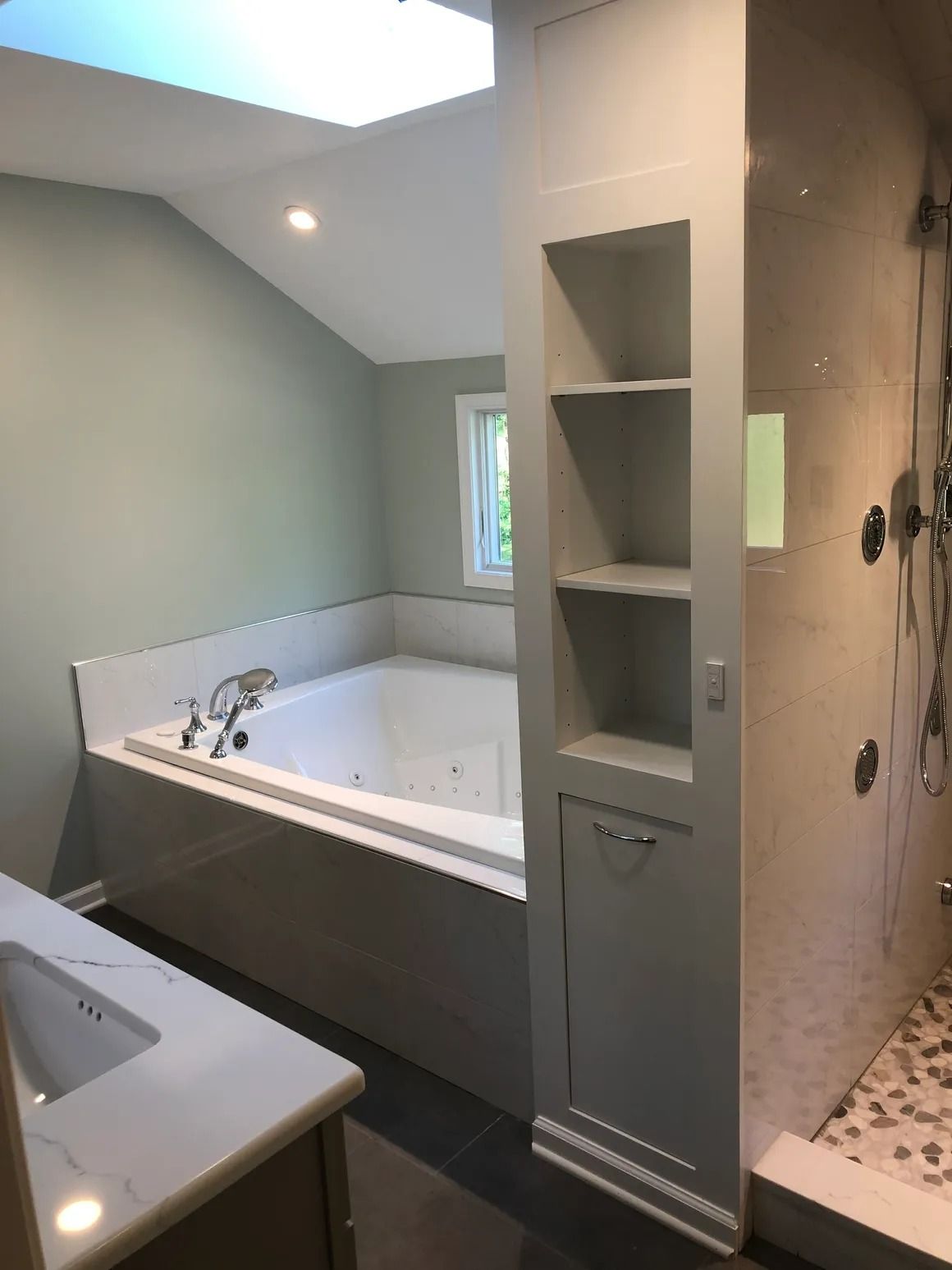Bathroom with a built-in tub, shelves, and a walk-in shower. Gray and white color scheme.