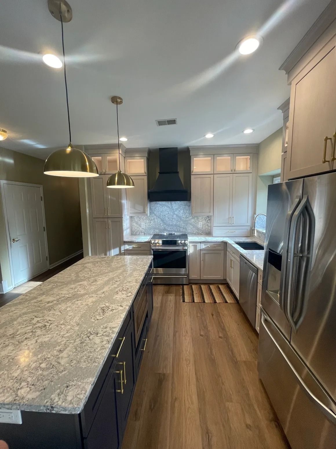 Kitchen with light cabinets, dark island, stainless steel appliances, pendant lights, and wood-look flooring.