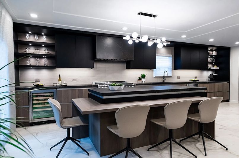 Modern kitchen with black and wood cabinets, island with seating, stainless steel appliances, and marble flooring.