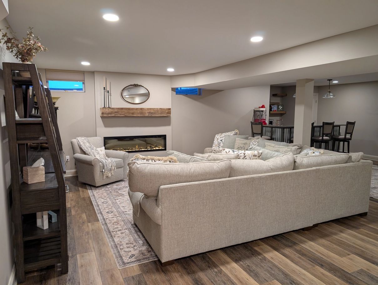Cozy basement living area with a fireplace, light gray couches, and wooden shelving.