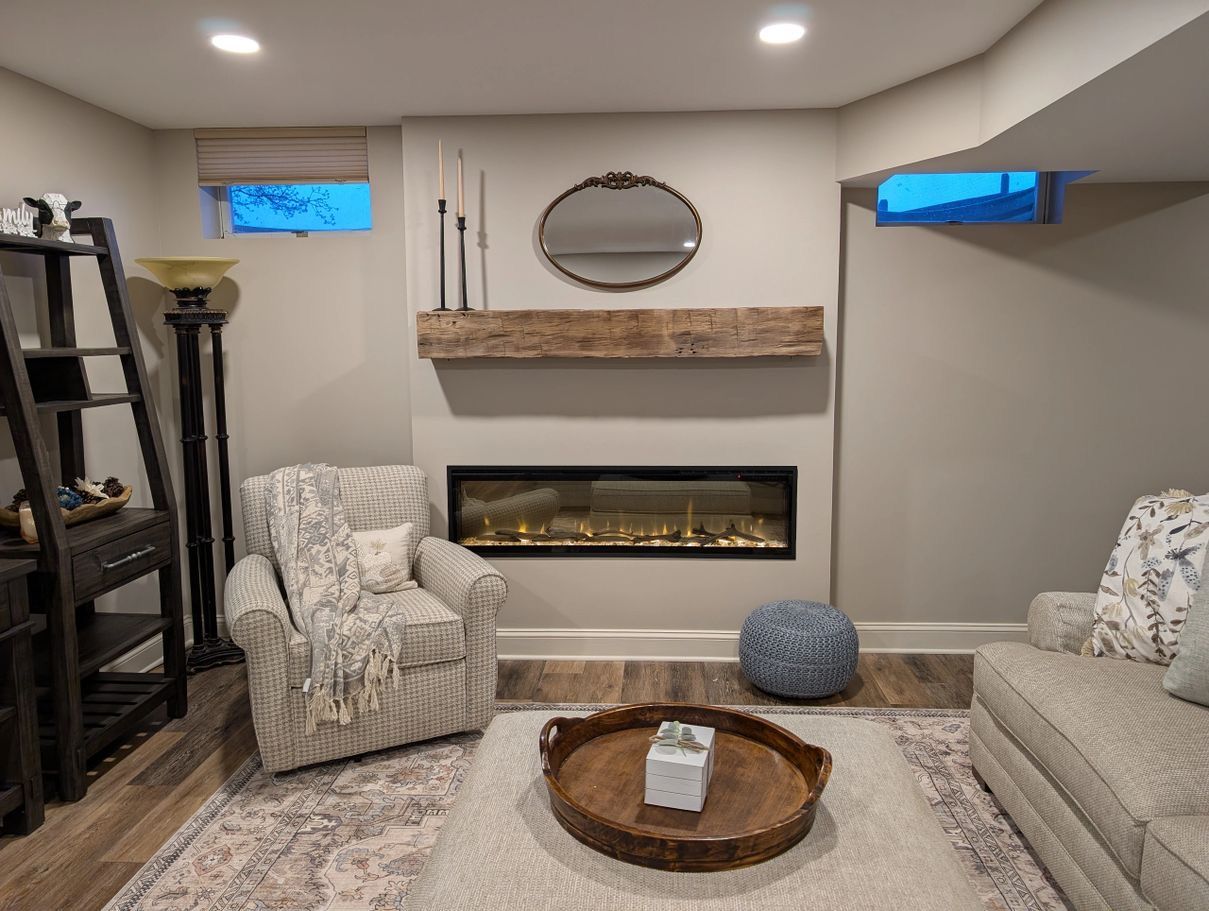 Cozy living room with fireplace, beige walls, rustic wooden mantel, two armchairs, and a decorative rug.