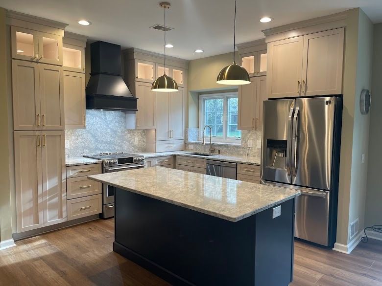 A renovated kitchen with light-colored cabinets, a black range hood, a dark island, and stainless steel appliances.