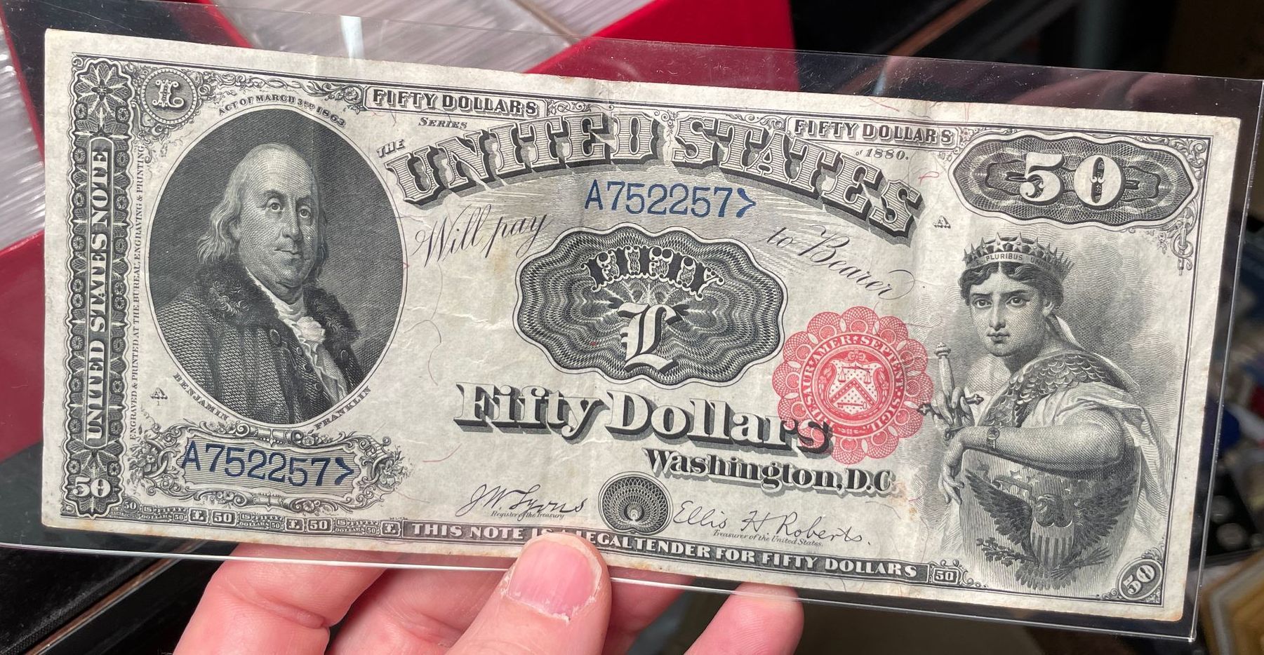 A worn old 50-dollar banknote held in a hand, with portraits on both sides.