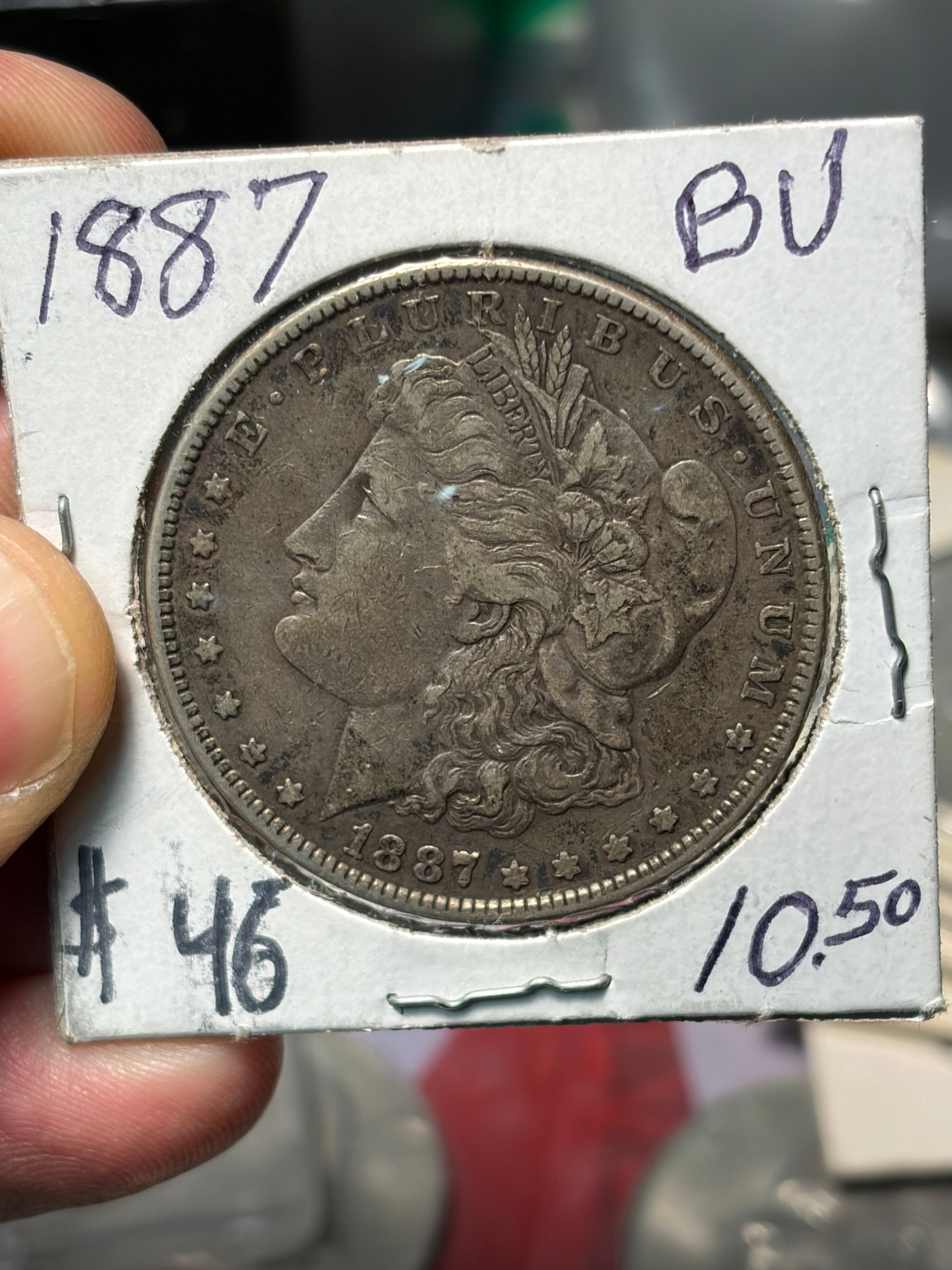 1887 silver coin in a holder labeled BU, with price $46 and $1050 noted on the card.