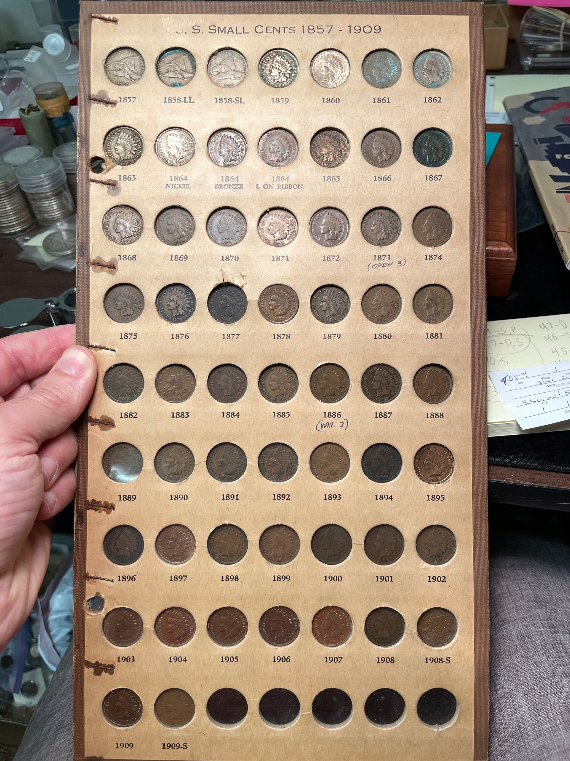 Hand holding a wooden tray with rows of small round metal discs, like coins or tokens