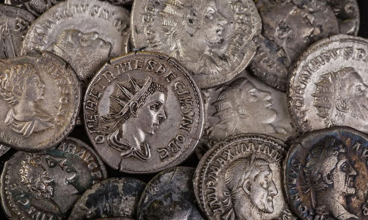Assorted worn silver coins with embossed profiles, tightly stacked and overlapping