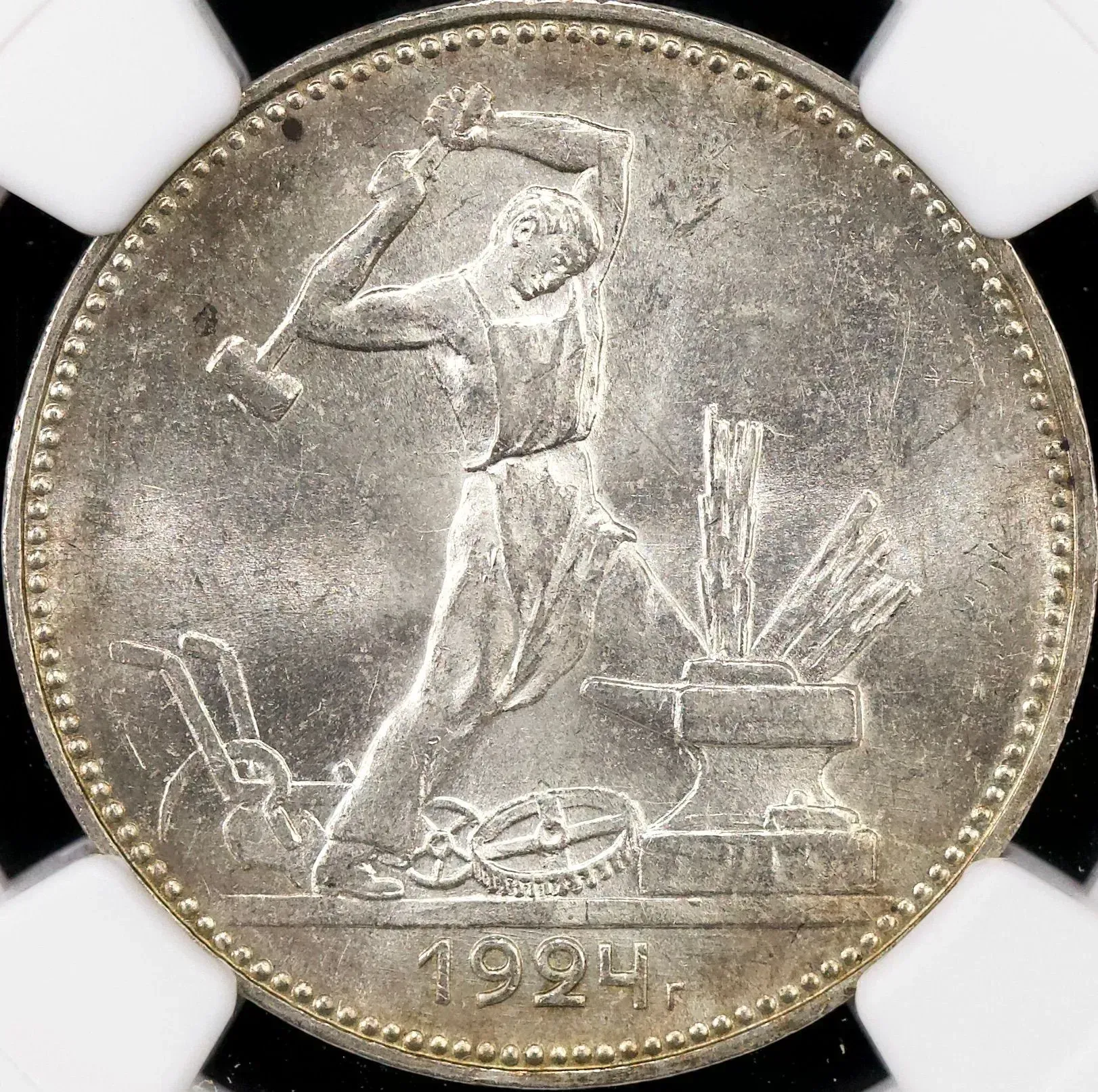 Silver 1924 coin with a standing figure, tools and an anvil, shown in close-up