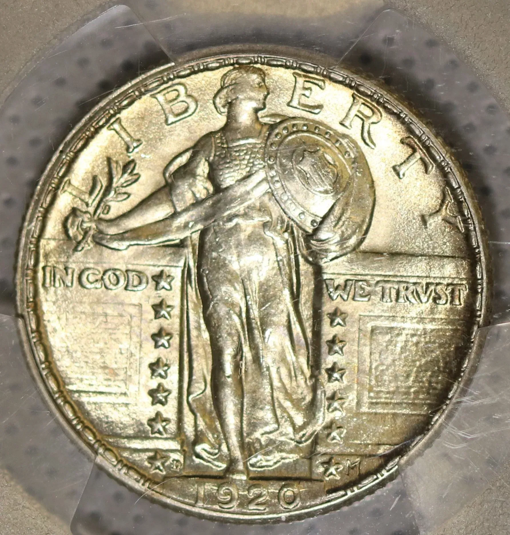 Close-up of a worn silver Standing Liberty quarter coin, dated 1920, in a clear holder.