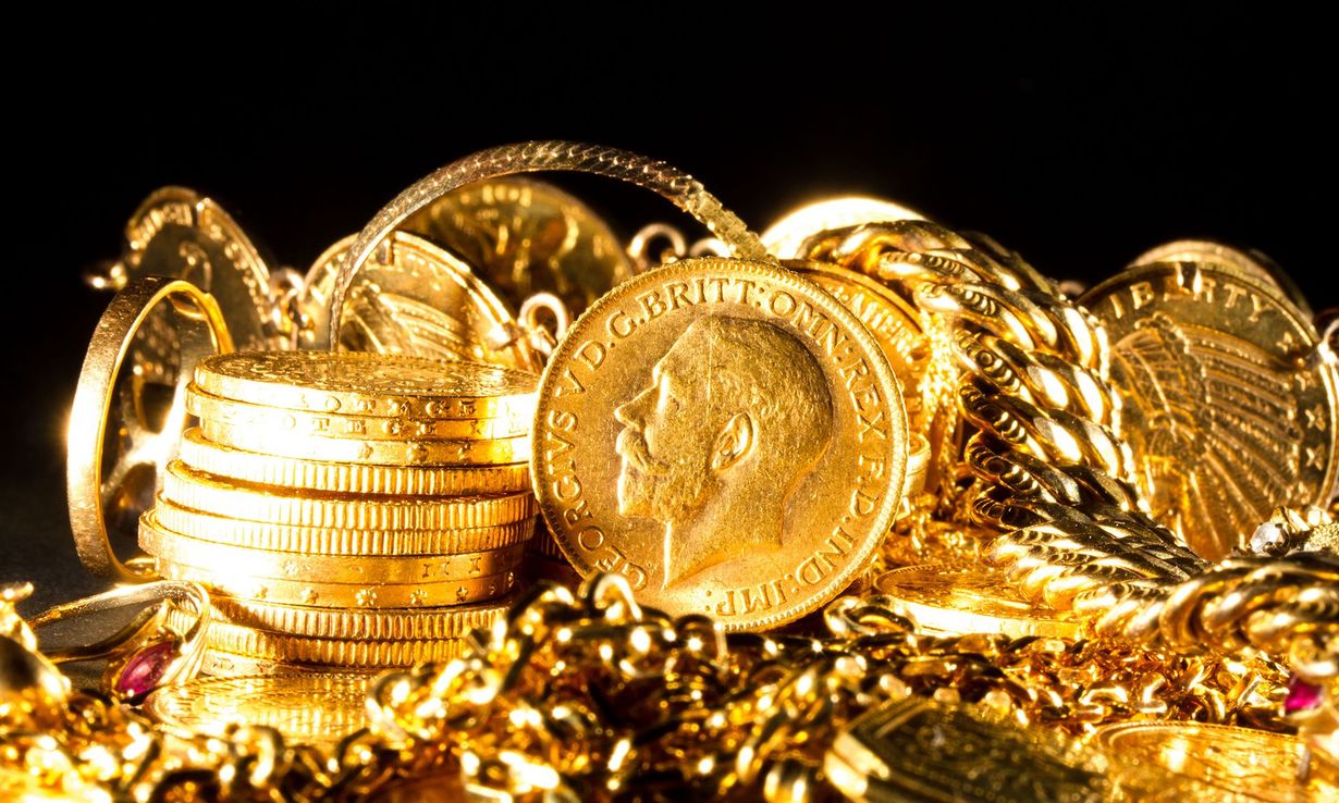 Stacks of gold coins and jewelry sparkling on a reflective surface in warm light