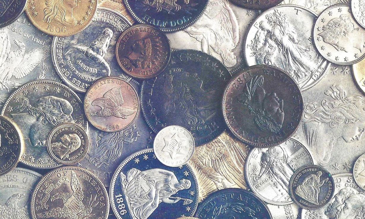 Scattered assorted coins in silver, copper, and dark tones on a textured surface